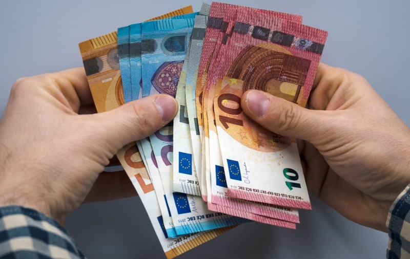 O persoană care ține bancnote de euro în mână