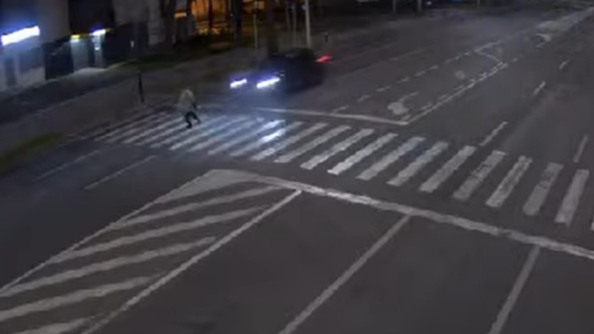 Imaginea surprinde un accident rutier petrecut noaptea, pe un bulevard larg din Iași. Se vede o trecere de pietoni iluminată, pe care un bărbat traversează, în timp ce un autoturism se apropie cu viteză mare, farurile fiind puternic vizibile. Atmosfera este una tensionată, cadrul sugerând momentul critic imediat înainte de impact.