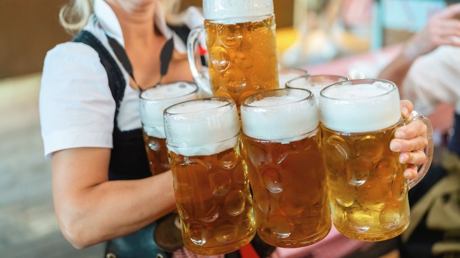 O chelneriță îmbrăcată în costum tradițional bavarez, ținând și transportând mai multe halbe de bere într-un cort de la Oktoberfest din München, Germania