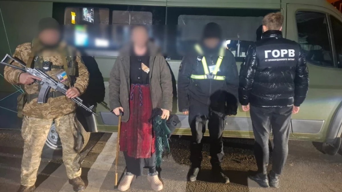 Doi bărbați, dintre care unul îmbrăcat în femeie stau între doi polițiști de frontieră ucraineni, după ce au fost depistați că voiau să treacă ilegal frontiera în Republica Moldova, 2 martie 2026