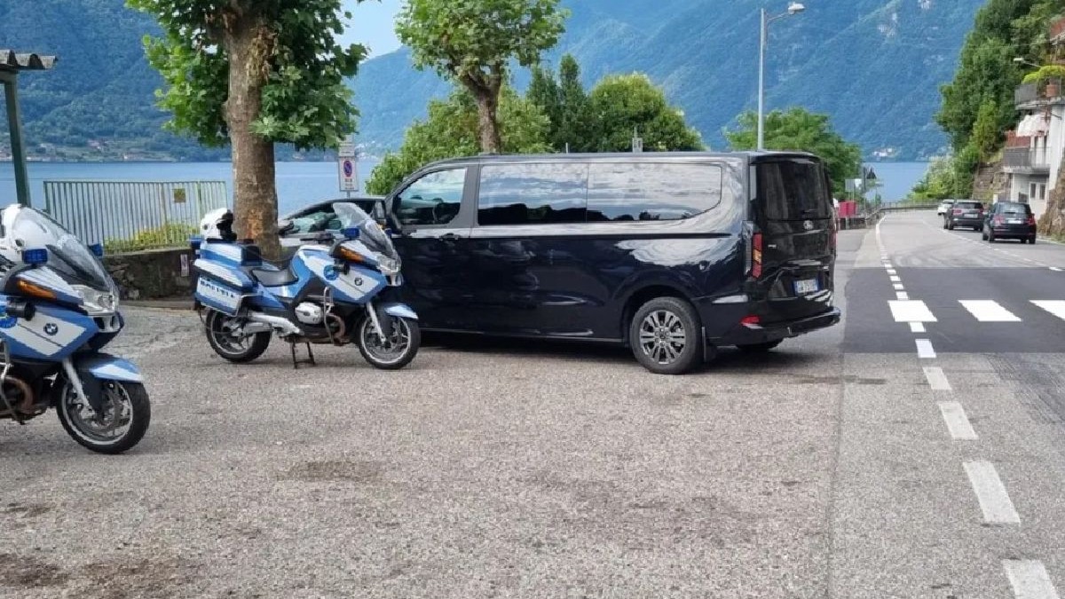 Imagine ilustrativă cu două motociclete de poliție și o dubă închisă la culoare sunt parcate lângă un drum cu un lac și munți ca fundal