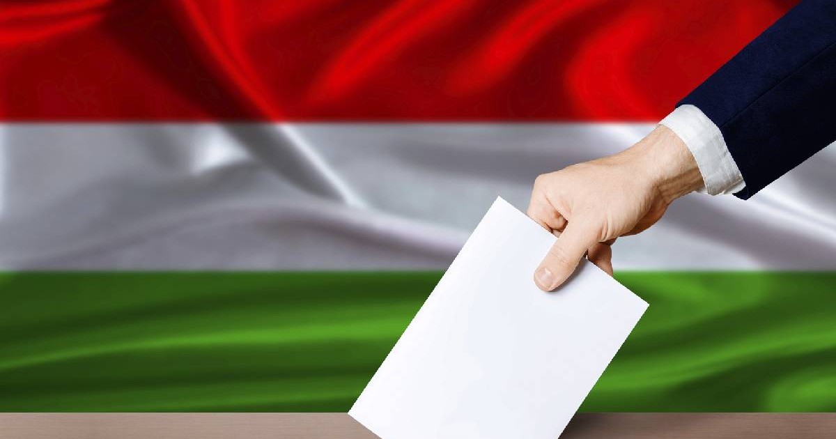 Kéz szavazólapot helyez az urnába, a háttérben a magyar zászló. 2026-os magyar parlamenti szavazás