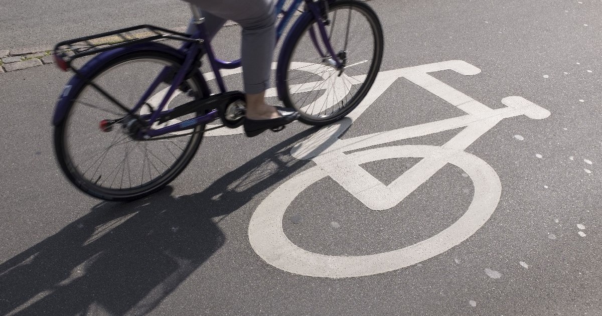 Pista de bicicleta, se vede o parte dintr-o bicicleta pe care merge o femeie imbracata in pantaloni gri și care poarta niste pantofi fara toc, negri