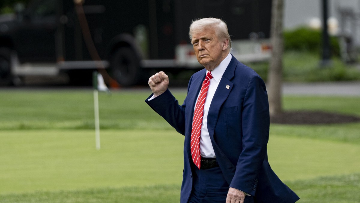 Donald Trump surprins în timp ce ține pumnul strâns. Poartă un costum albastru, cu cămașă albă și cravată roșie