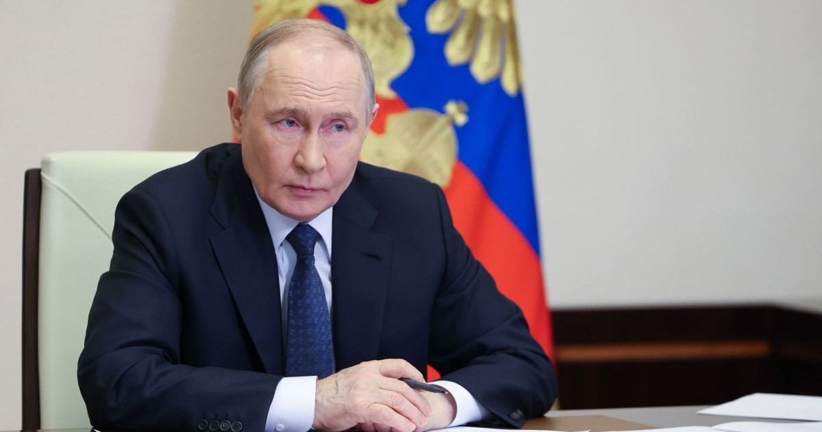 Vladimir Putin stă la birou cu un pix în mână și cu niște foi în față, având pe fundal steagul Federației Ruse, 7 aprilie 2026