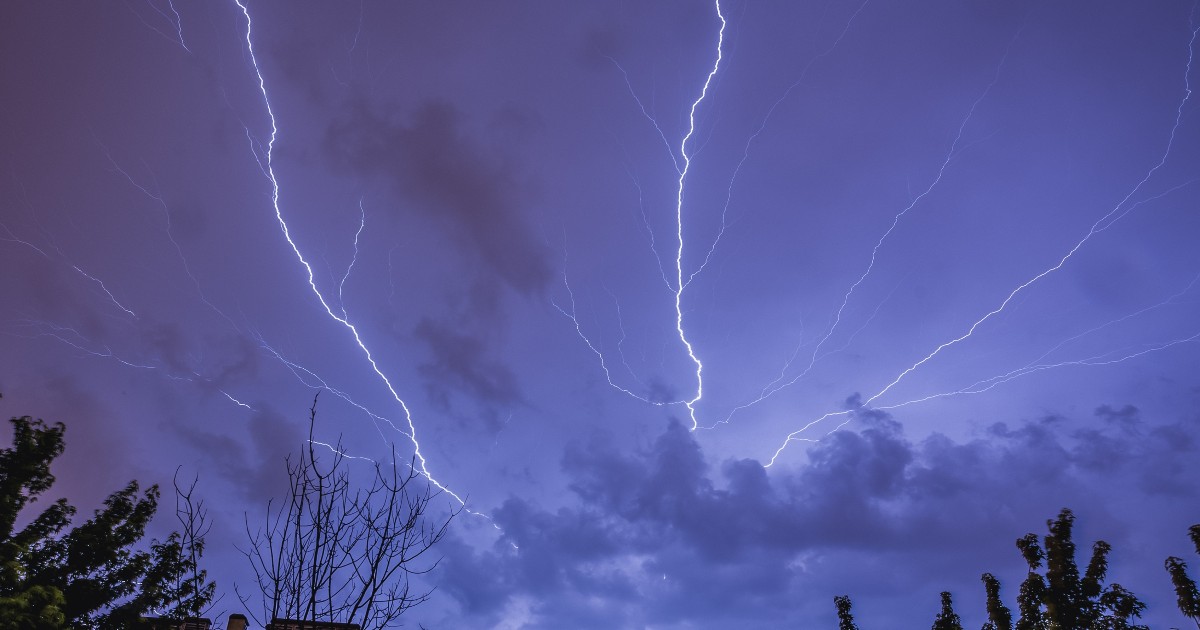 În imagine sunt ilustrate fulgere pe cer, pe timpul serii. În partea de jos a cadrului se disting copaci și clădiri.
