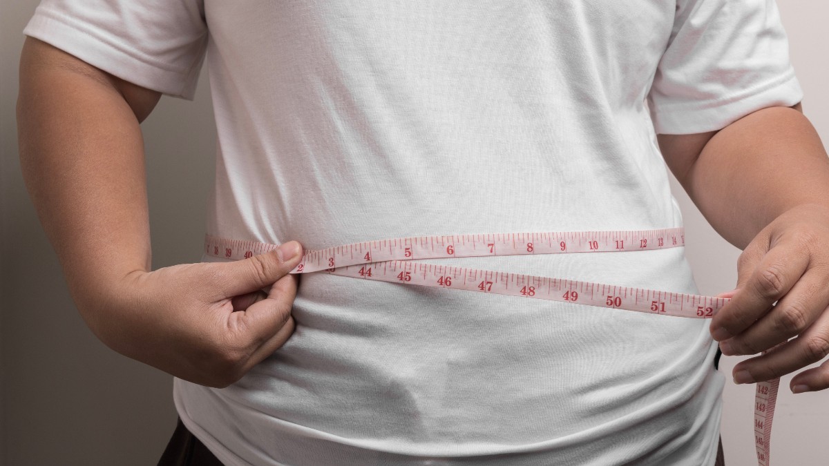 În imagine este ilustrată o femeie îmbrăcată în tricou alb, care își măsoară talia