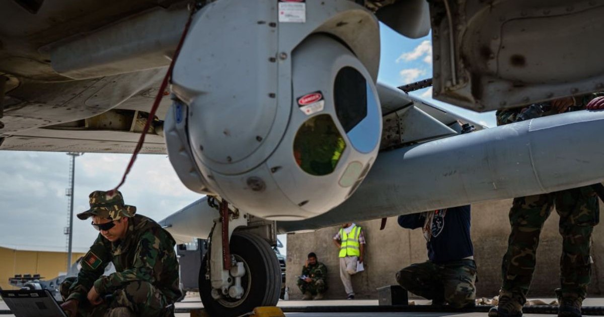 Sistemul american de apărare Merops, atașat de un avion de luptă. lângă sistem se află un militar, îmbrăcat în uniformă camuflaj, stând pe laptop, pe jos