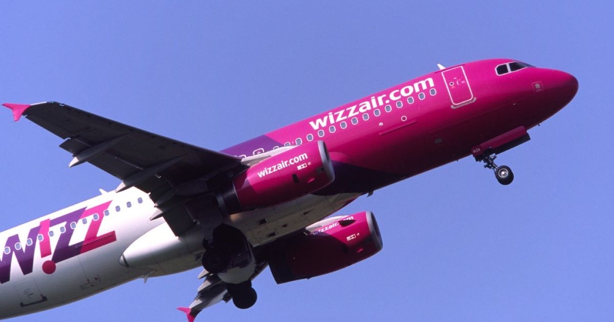 Un avion al companiei WizzAir, cu roz si alb, in zbor