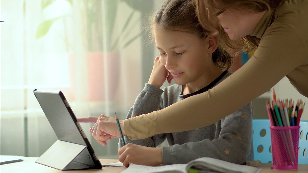 Un fată care învață în sistem homeschooling este ajutată de mama ei la teme