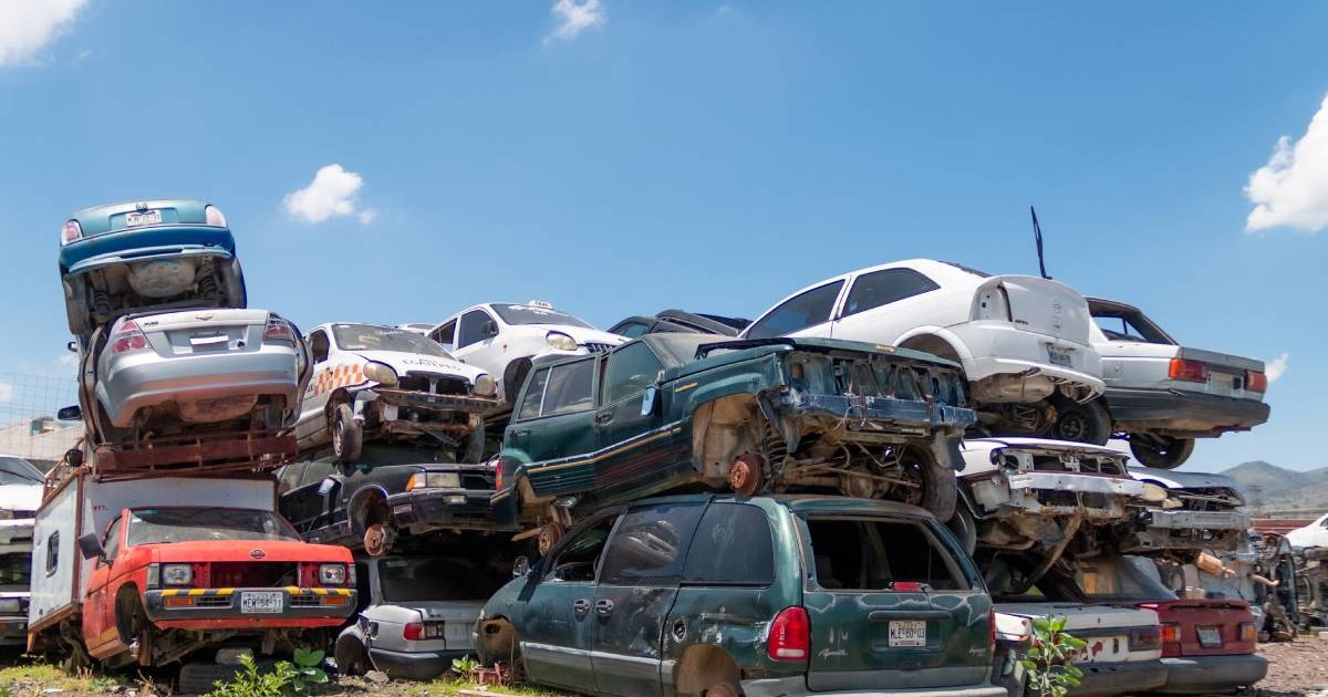 Parc auto de dezmembrări, unde mai multe mașini vechi sunt stivuite în grămezi, majoritatea deteriorate.