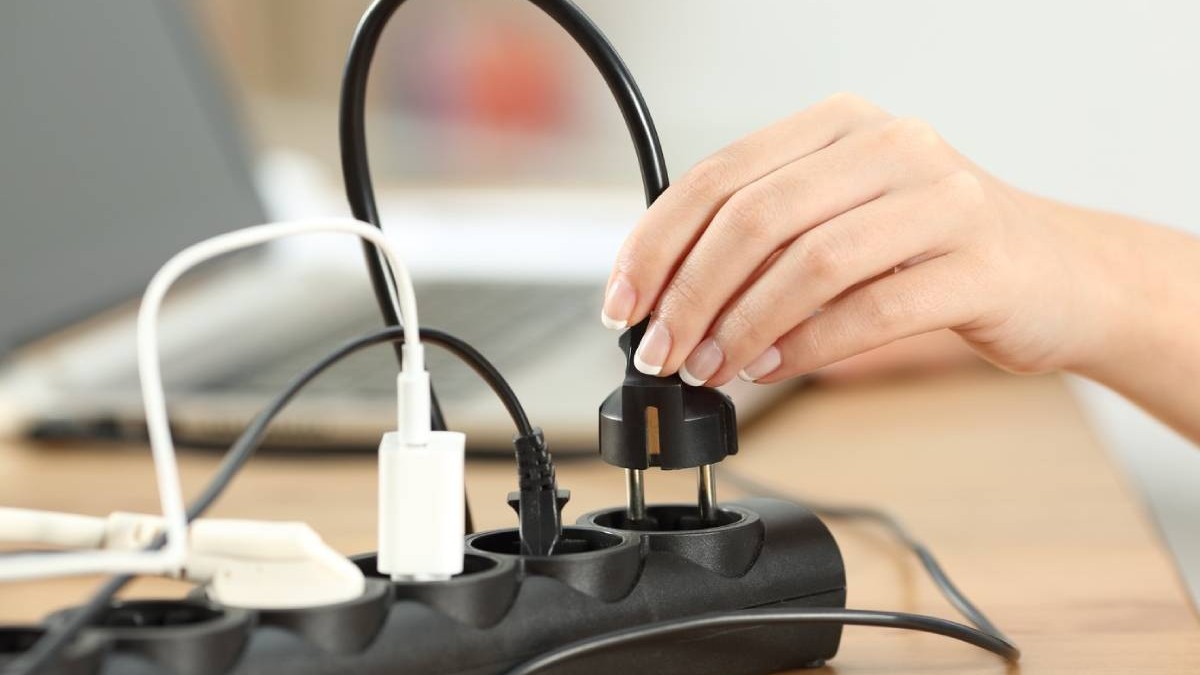 Prim-plan al mâinii unei femei care introduce un ștecher într-o priză electrică pe o masă acasă