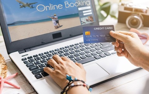 o persoană care folosește un laptop pentru a efectua o rezervare online, ținând un card de credit într-o mână și tastând cu cealaltă