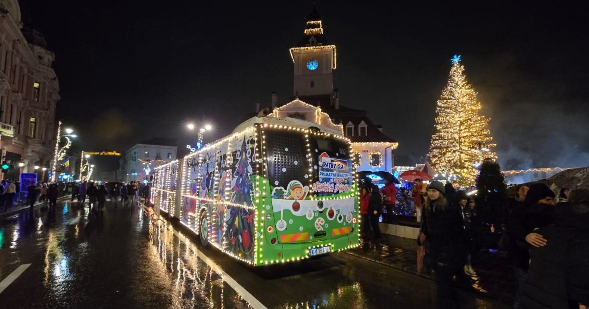 Imaginea surprinde Autobuzul lui Moș Crăciun, decorat festiv cu lumini și ilustrații tematice, aflat în centrul Brașovului, pe timp de seară. În fundal se văd clădiri istorice, bradul de Crăciun luminat și oameni adunați în zonă, creând o atmosferă de sărbătoare și poveste.