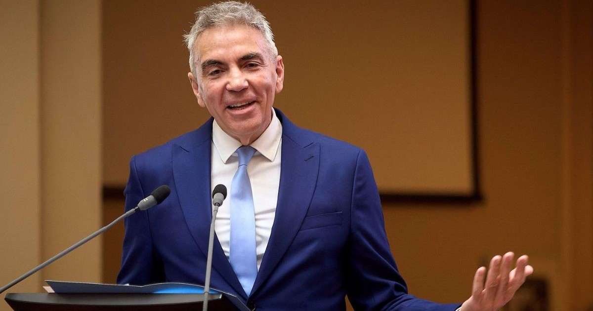 Dragoș Anastasiu, îmbrăcat într-un costum albastru închis, o cămașă albă și o cravată bleu, vorbind la un microfon la pupitru, cu mâinile larg deschise, în timpul unei conferințe de presă
