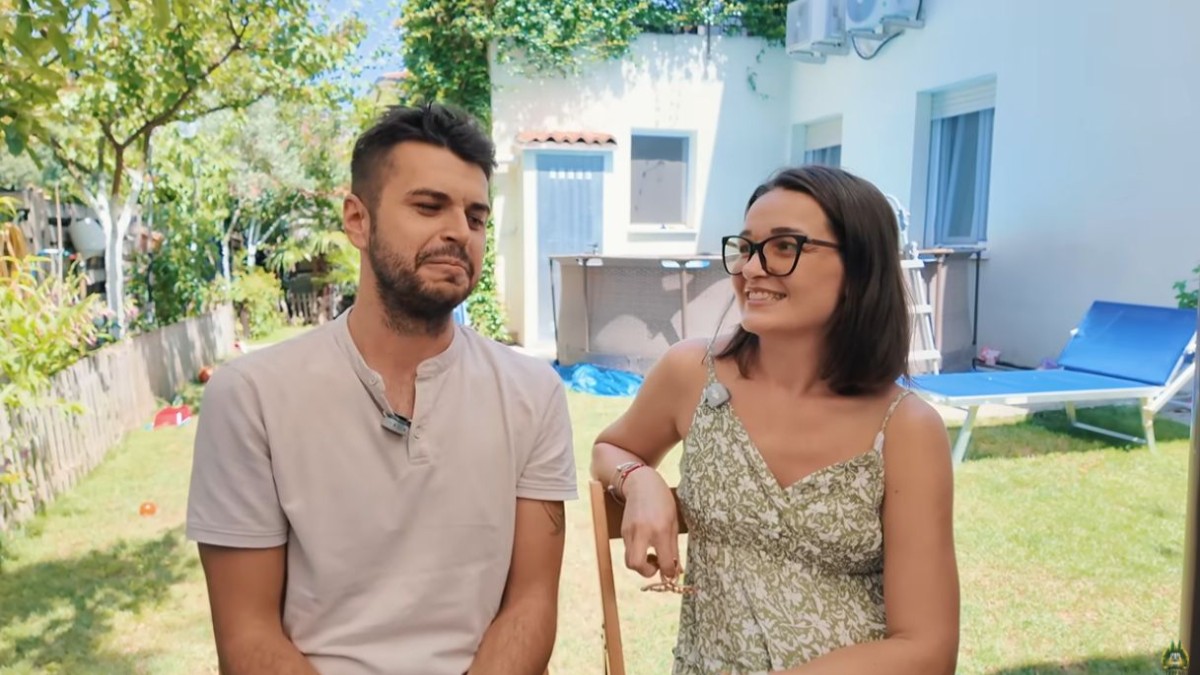 O femeie și un bărbat în timpul unui interviu, stau într-o grădină, în fața casei