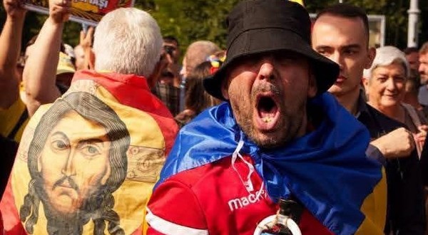 O imagine cu fața lui Isus pe un steag purtat pe spate de un protestatar, langa un al protestatar care tip la protestul fermierilor din Piața Victoriei, de pe 15 septembrie