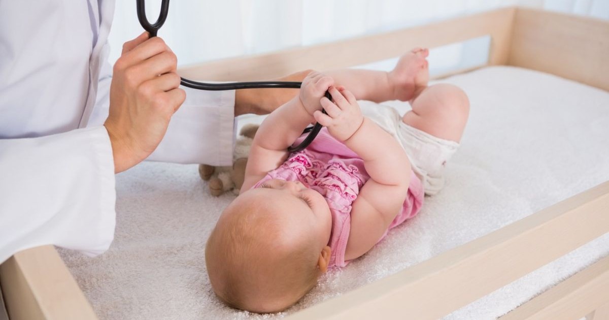 O fetiță care stă pe un pat de spital se joacă cu stetoscopul medicului care o consultă