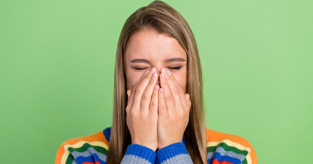 De ce nu poţi să strănuţi fără să închizi ochii - Imagine cu o femeie care strănută cu ochii închişi, ţinându-şi mâinile la gură şi nas
