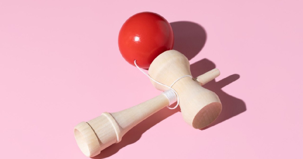O jucărie kendama de lemn, cu bilă roșie, pe un fundal roz