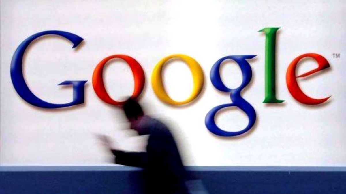 Google va plăti anumite trusturi de presă pentru știri de calitate. Om trecând prin fața unui logo Google