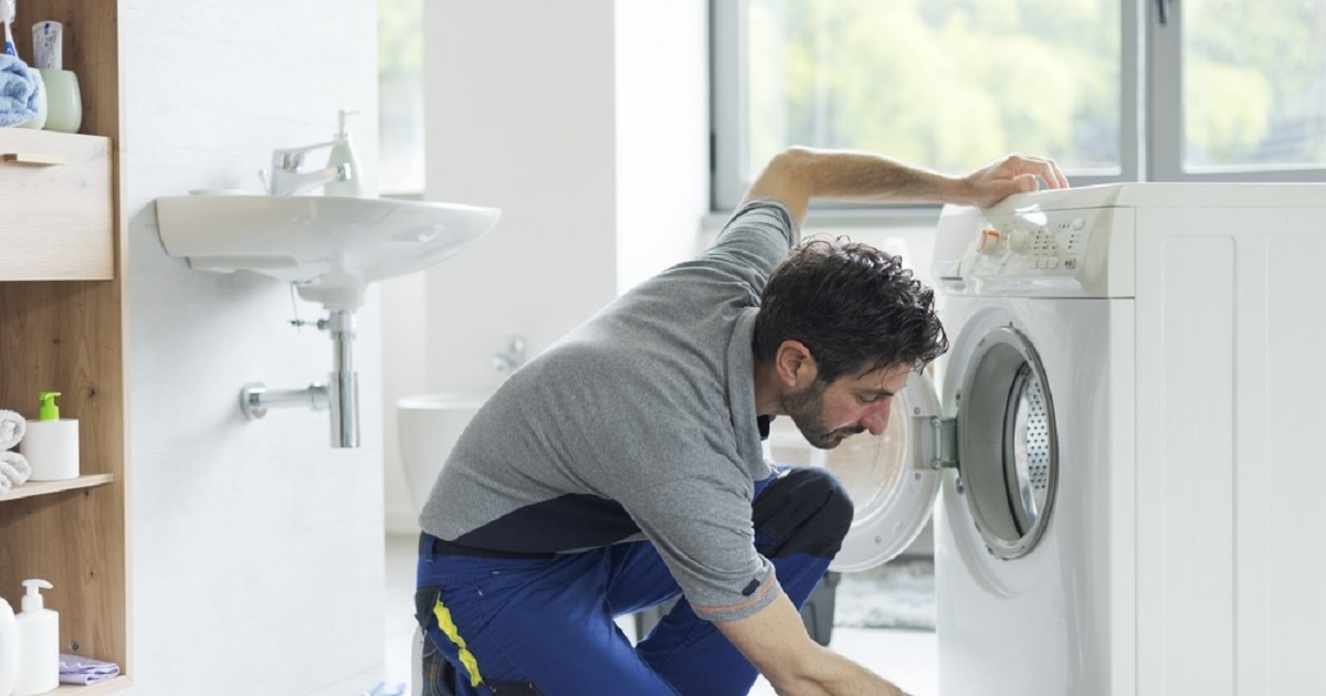Trucuri simple care prelungesc viața mașinii de spălat rufe - Imagine cu un tehnician care repară o maşină de spălat rufe