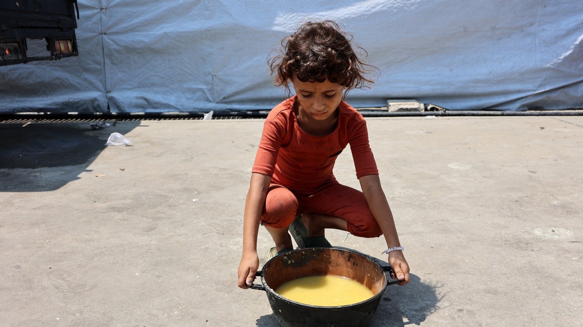 Imagine cu o fetiță care privește o oală cu mâncare, în Gaza (25 iulie 2025). Poartă o bluză roșie și pantaloni de aceeași culoare