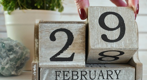 Calendar din lemn care arată data de 29 februarie, cu o mână ce mută un bloc de la 28 la 29.