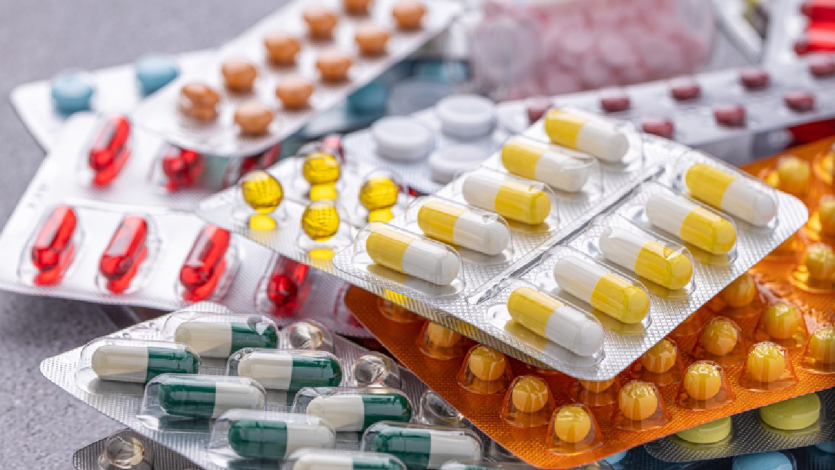 Imaginea este un prim-plan cu focalizare superficială care arată o grămadă de blistere de medicamente de diverse culori și forme, inclusiv capsule albe și galbene, pastile rotunde roșii și tablete maro. Abundența și varietatea blisterelor sugerează o gamă largă de produse farmaceutice disponibile.