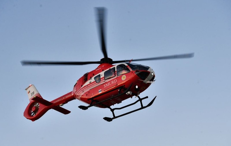 Elicopter SMURD, de culoare roșie, aflat în zbor, cu cerul albastru pe fundal