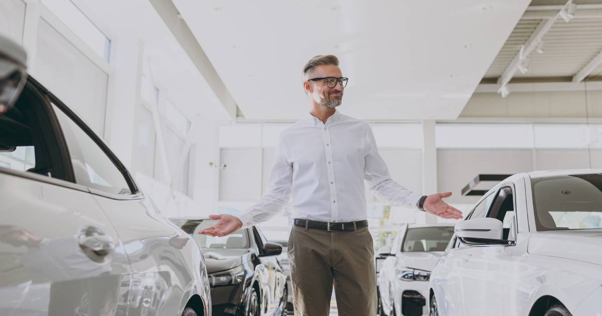 barbat imbracat cu o camasa alba aflat printre mai multe masini intr-un showroom auto