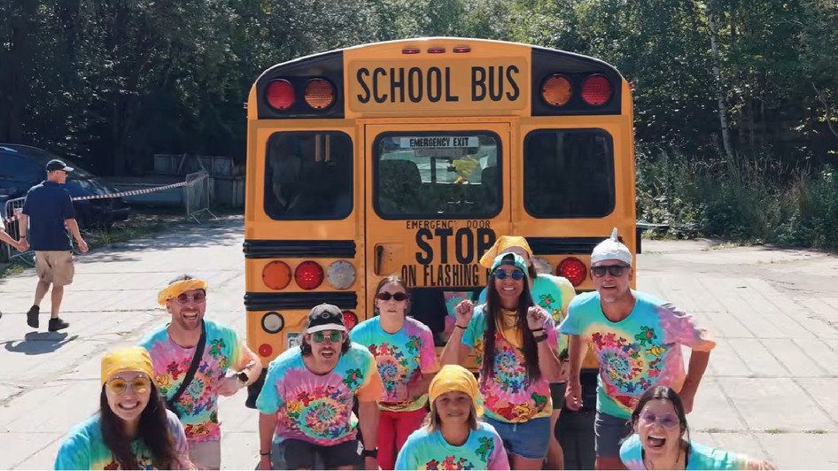 9 americani imbracati in tricouri colorate pozeaza langa un autobuz galben scolar din SUA