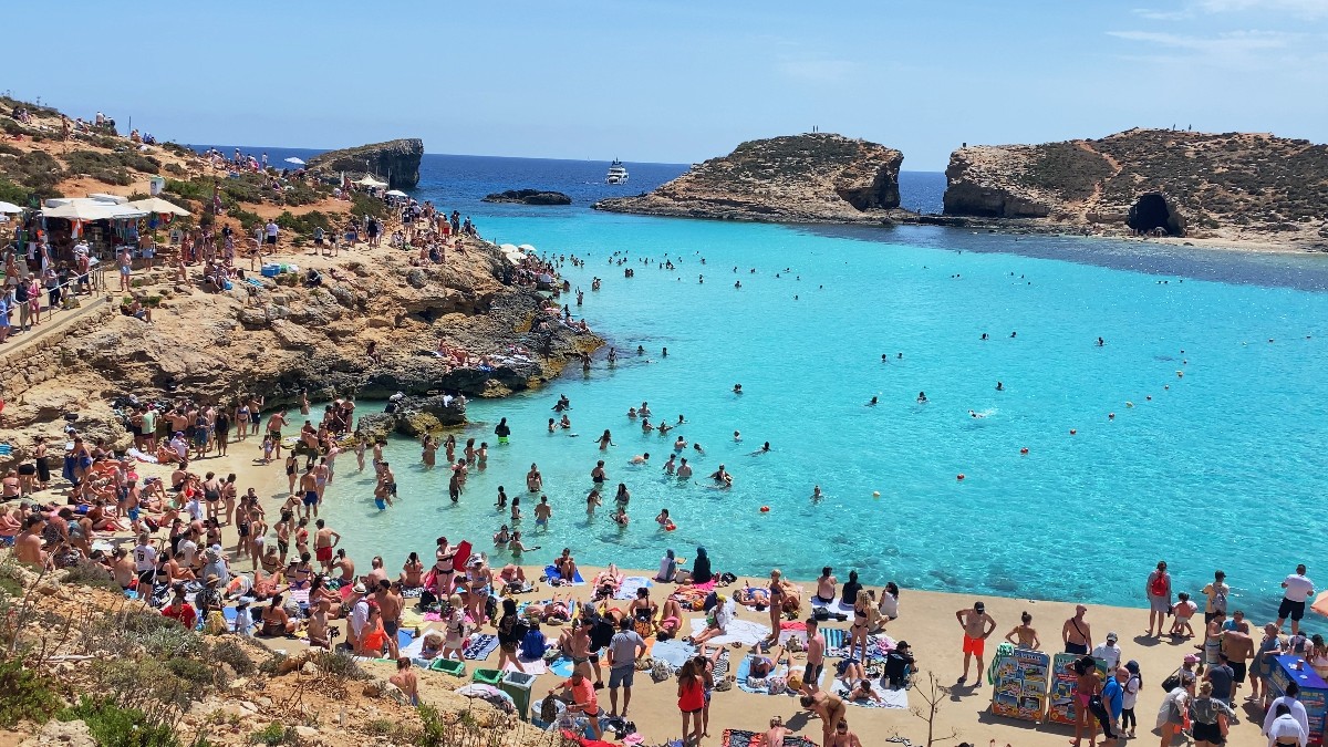 O plajă din Malta, plină de turiști veniți să facă baie printre stânci, în apa turcoaz a mării