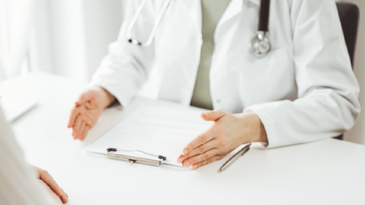 Doctorul și pacientul stând și discutând ceva unul lângă celălalt la biroul alb din clinică