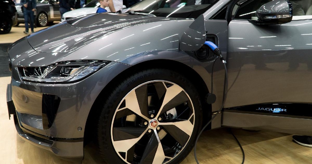 Gemini a spus Imaginea surprinde un Jaguar I-PACE, primul model complet electric al mărcii britanice, într-o nuanță elegantă de gri închis metalizat. Mașina este expusă la un salon auto sau într-un showroom, pe o podea din lemn deschis la culoare.