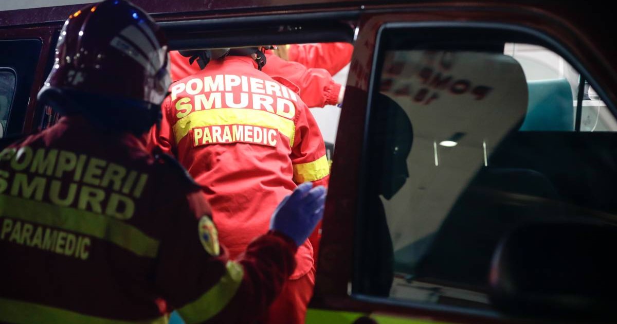 Doi medici din echipajul SMURD în timp ce intră în ambulanță, aceștia poartă căști pe cap și uniforme roșii