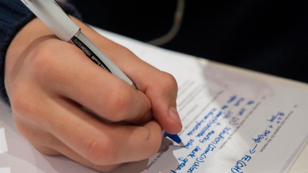 Un băiat cu un pic în mână scrie pe o hârtie rezolvarea unor exerciții