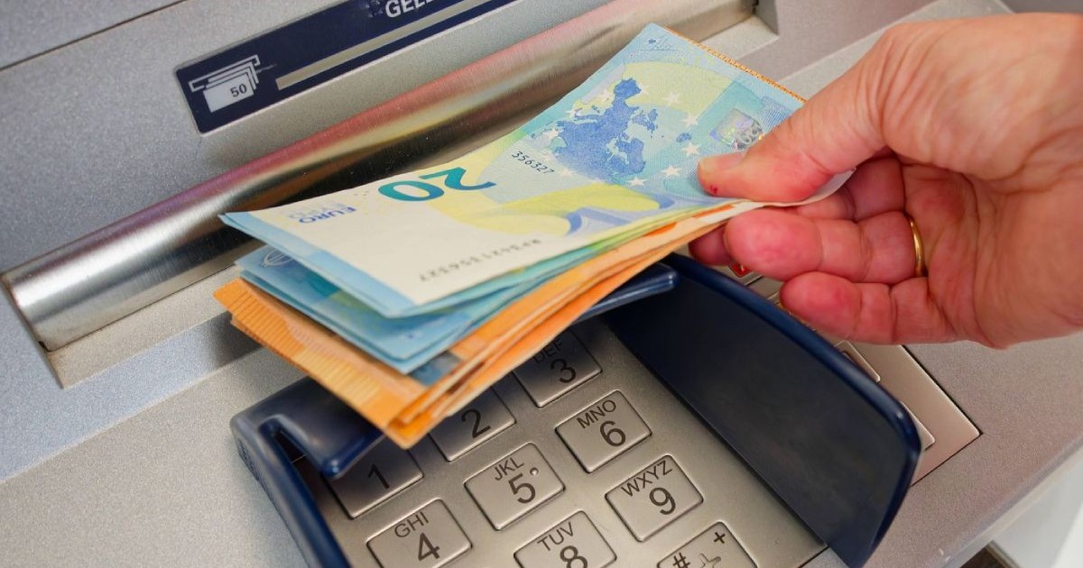 Bancnote de euro, de 20 și 50 de euro, ținute într-o mână, în fanta de retragere a unui bancomat