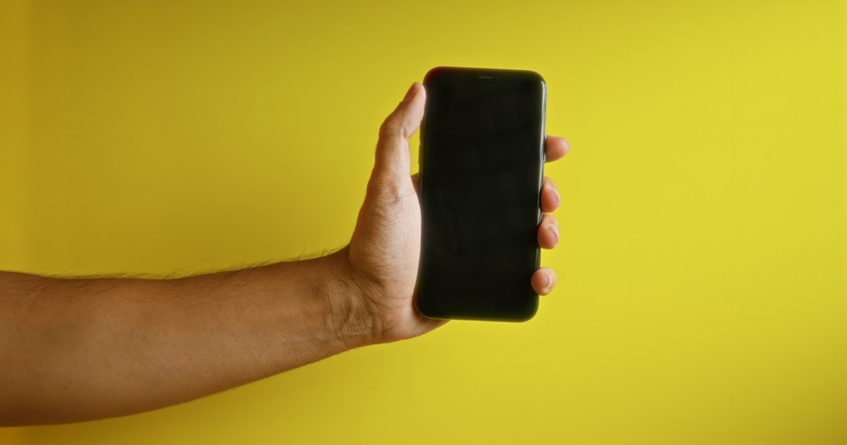 Telefoane sub 1.000 de lei la eMAG de Black Friday 2024 - Imagine cu un smartphone ţinut de o mână de bărbat pe un fond galben
