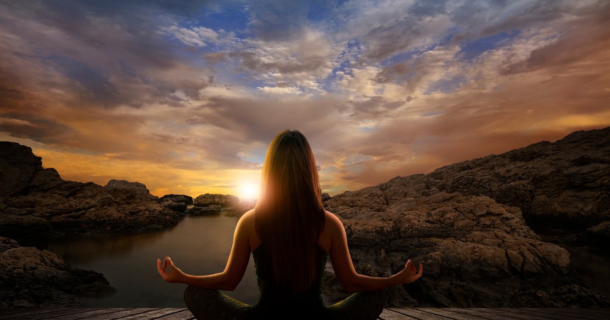 Diferența dintre meditație și mindfulness - Imagine cu o femeie care meditează în faţa unui peisaj cu un apus de soare