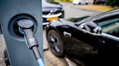 Electric car plugged in and charging at a streetside station.