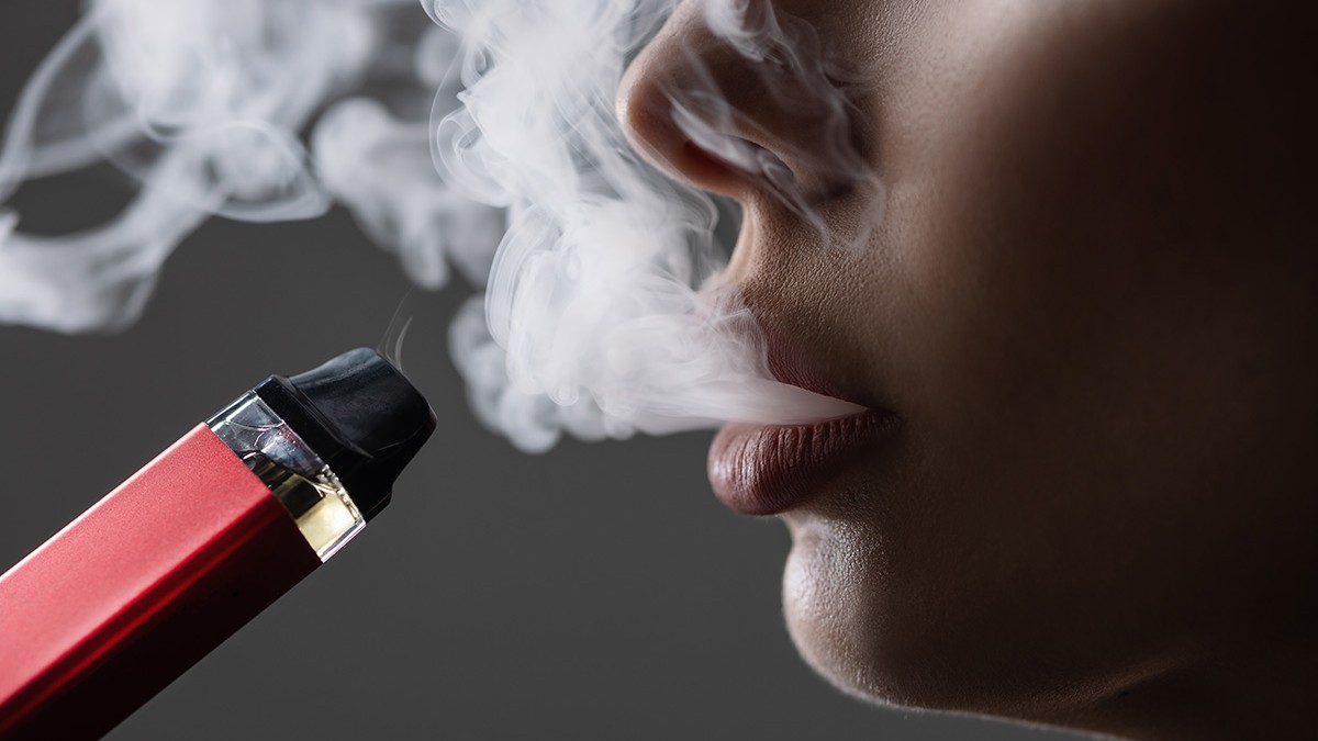 Un plan apropiat cu gura unei persoane care expira și inhalează aburi dintr-o tigare electronică grena.