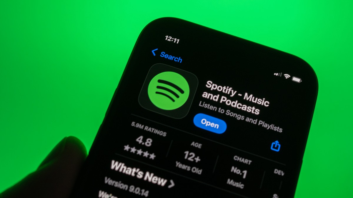 Pagina aplicației SPotify din AppStore, deschisă pe ecranul unui iPhone ținut în mână în fața unui fundal verde.