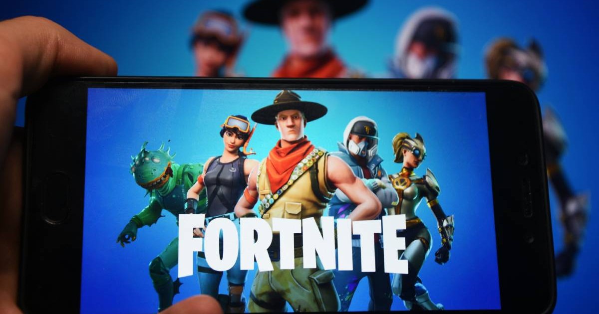 Personajele din Fortnite și logo=ul jocului apar pe eranul unui telefon mobil pe care un băiat în ține în mână
