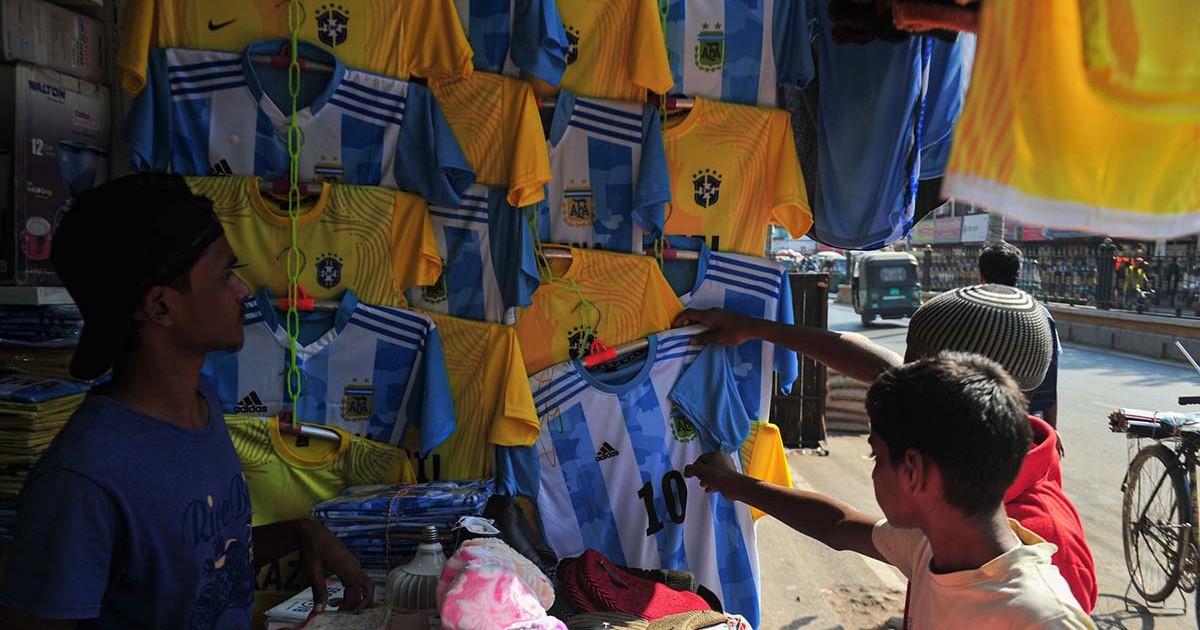 Doi copii privesc tricourile Argentinei expuse de un vânzător la o tarabă.
