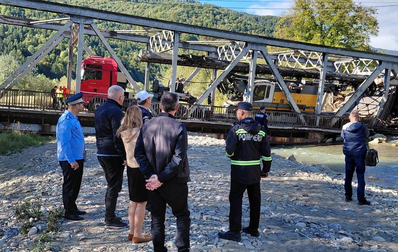 Mai multe persoane privesc la un pod metalic care a fost distrus de greutatea unui camion care transporta o macara