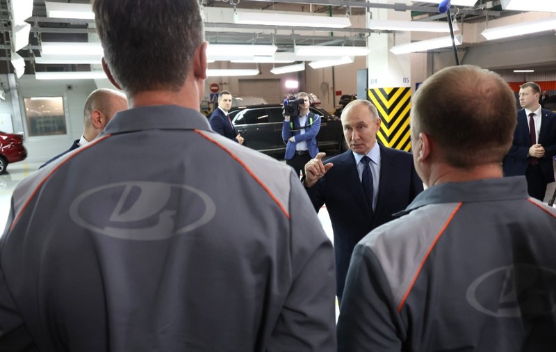 Președintele rus Vladimir Putin discutând cu angajați purtând uniforme marca Lada, în interiorul unei fabrici auto.   