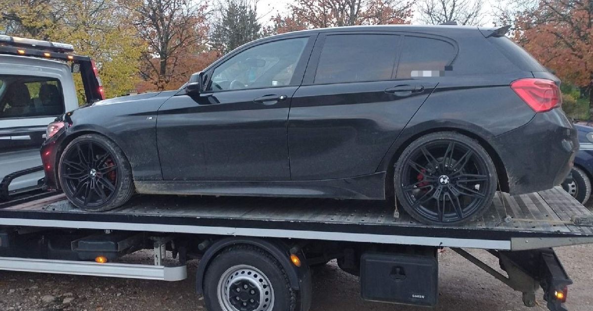 Imaginea arată un BMW negru transportat pe o platformă de remorcare