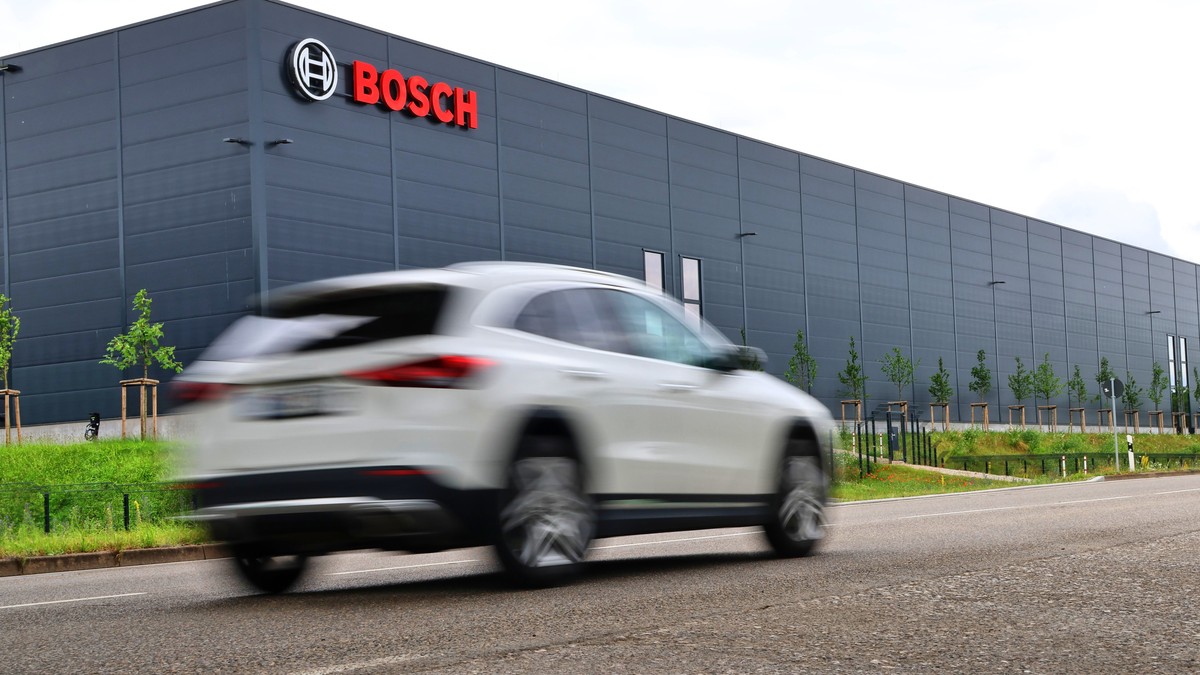 Fabrică Bosch cu logo-ul companiei prin fața căruia trece un Audi alb