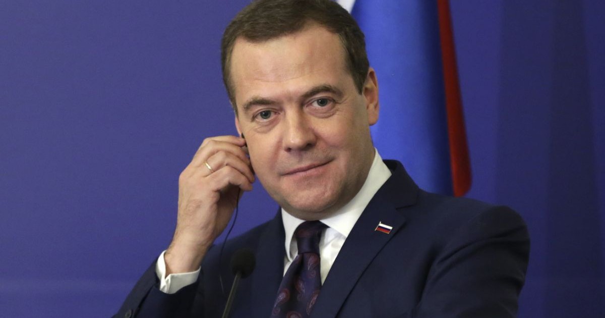 Dmitry Medvedev in costum negru si cravata, cu mana dreaptă la ureche